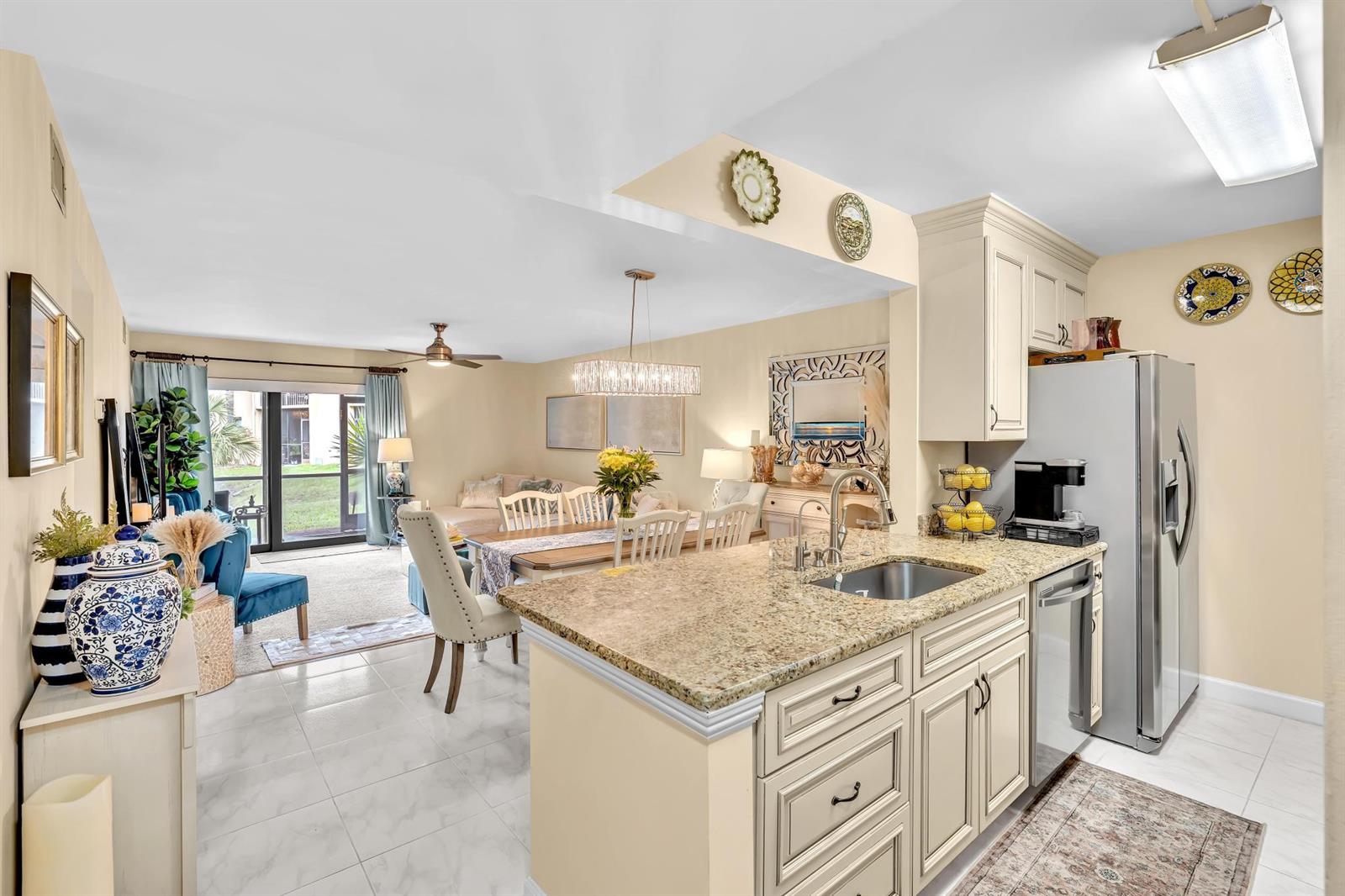 A kitchen with granite countertops and white cabinets overlooks an open-concept dining and living area — 912 SW 9th Street Circle # 105, Boca Raton FL 33486, BOCA RATON, FL