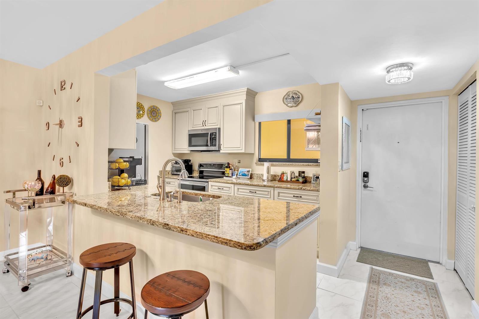 A kitchen with granite countertops, light-colored cabinets, a breakfast bar, and an adjacent entryway door — 912 SW 9th Street Circle # 105, Boca Raton FL 33486, BOCA RATON, FL