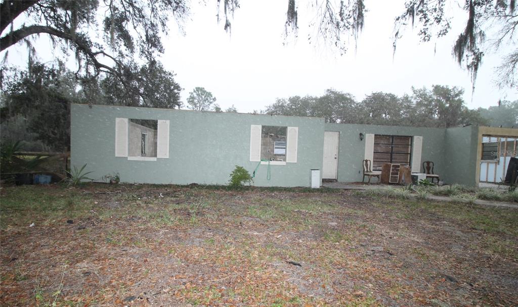 A single-story house exterior features missing windows, exposed framing, and a large yard — 8725 TREASURE ISLAND ROAD, LEESBURG, FL
