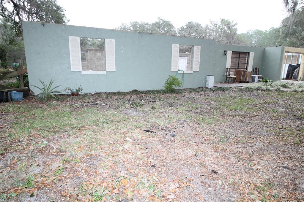 The exterior of a single-story house with missing windows and a partially unfinished wall section — 8725 TREASURE ISLAND ROAD, LEESBURG, FL