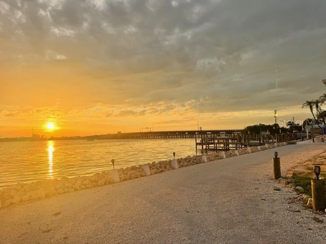A gravel path runs along a waterfront at sunset with a bridge in the distance — 12507 CORTEZ ROAD W UNIT 56, CORTEZ, FL