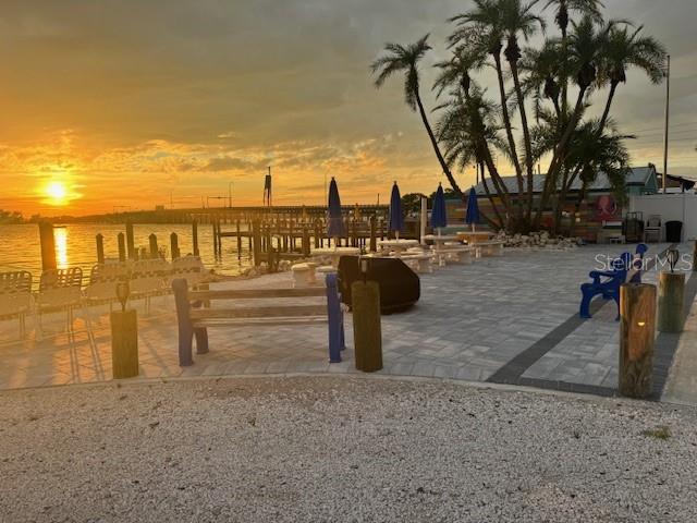 An outdoor patio with pavers, benches, and palm trees overlooks a sunset over the water — 12507 CORTEZ ROAD W UNIT 56, CORTEZ, FL