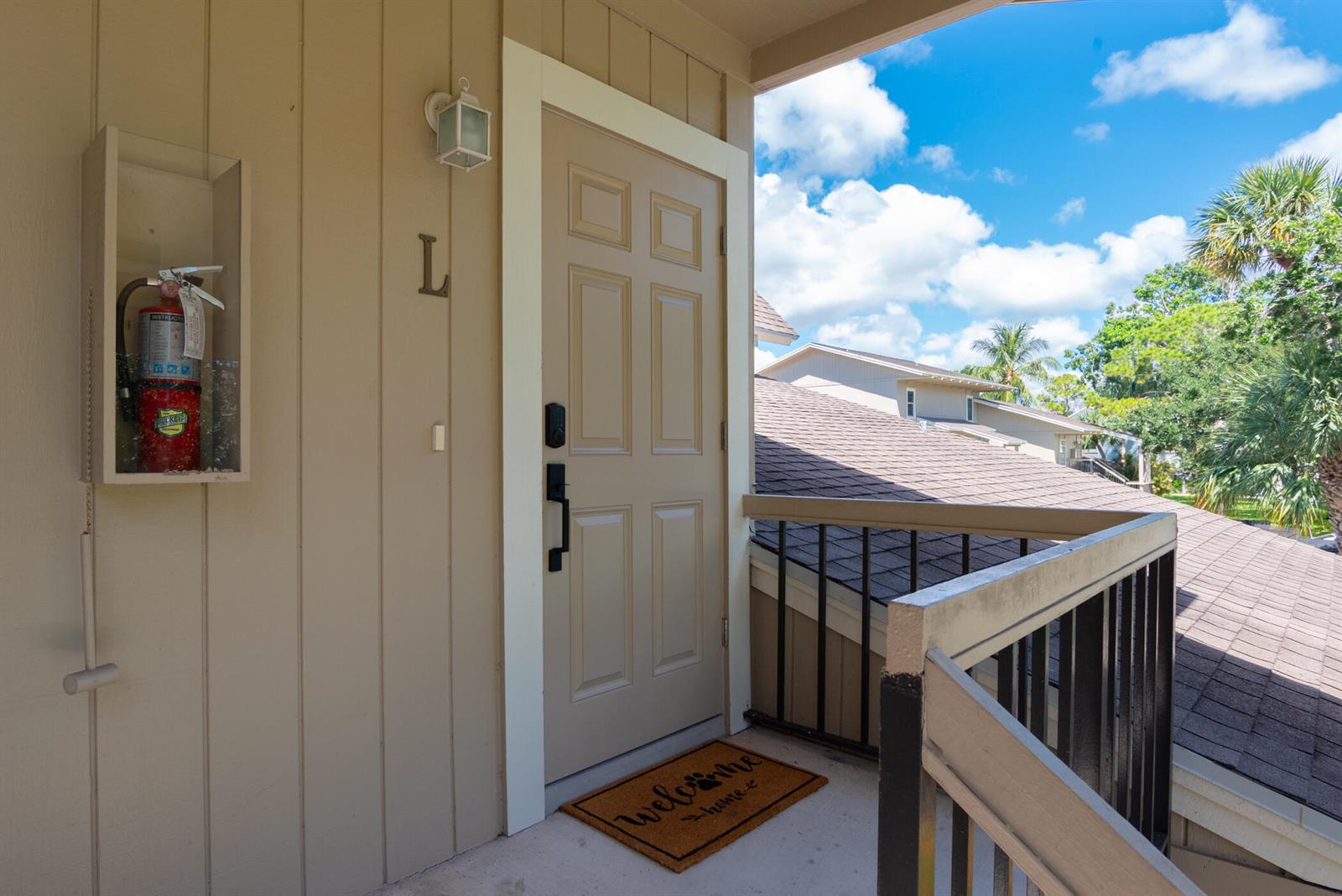An exterior view of a tan apartment door with a fire extinguisher and welcome mat — 9130 SE Riverfront Terrace # L, Jupiter FL 33469, JUPITER, FL