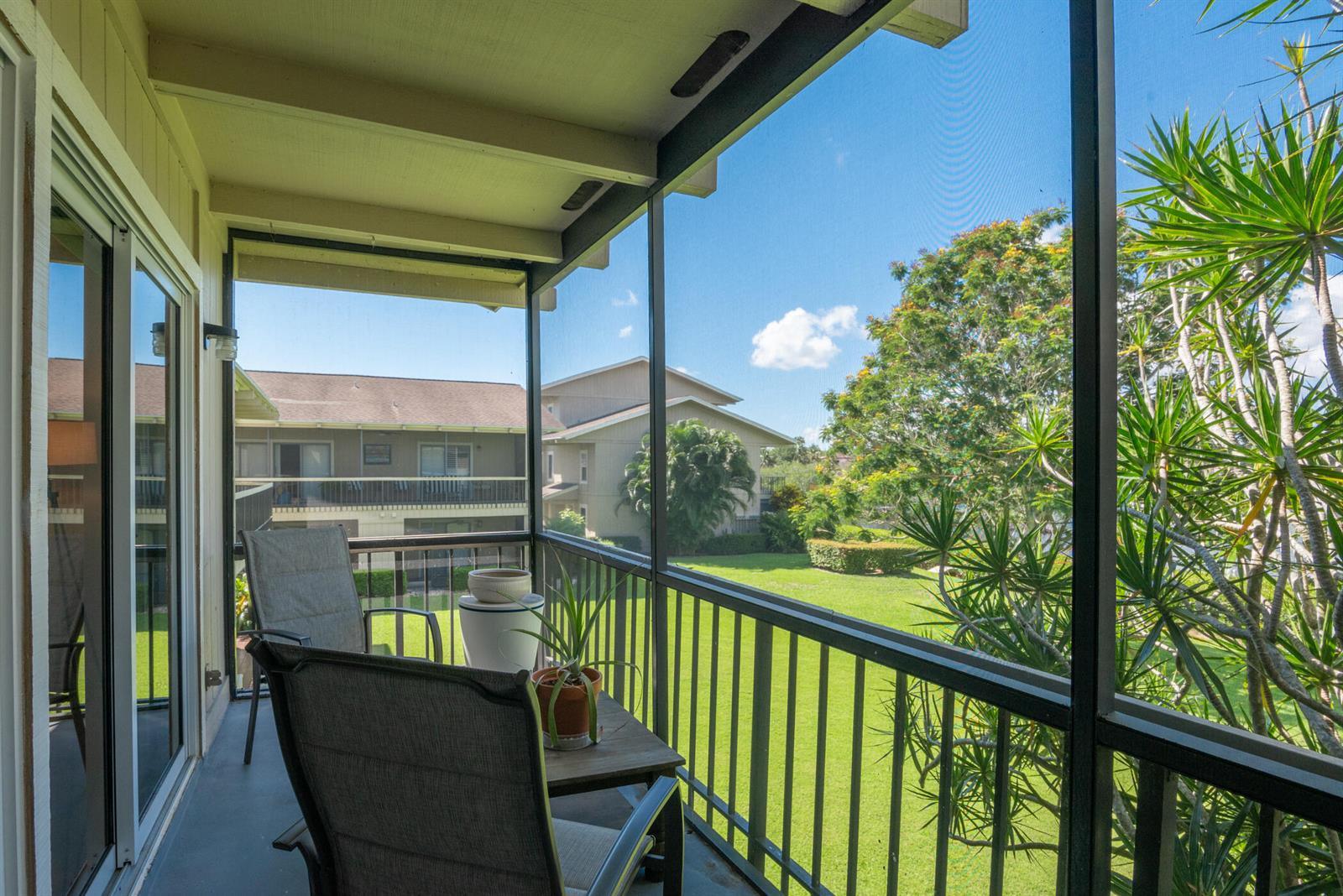 A screened-in balcony features two chairs, a small table with a plant, and a lawn view — 9130 SE Riverfront Terrace # L, Jupiter FL 33469, JUPITER, FL