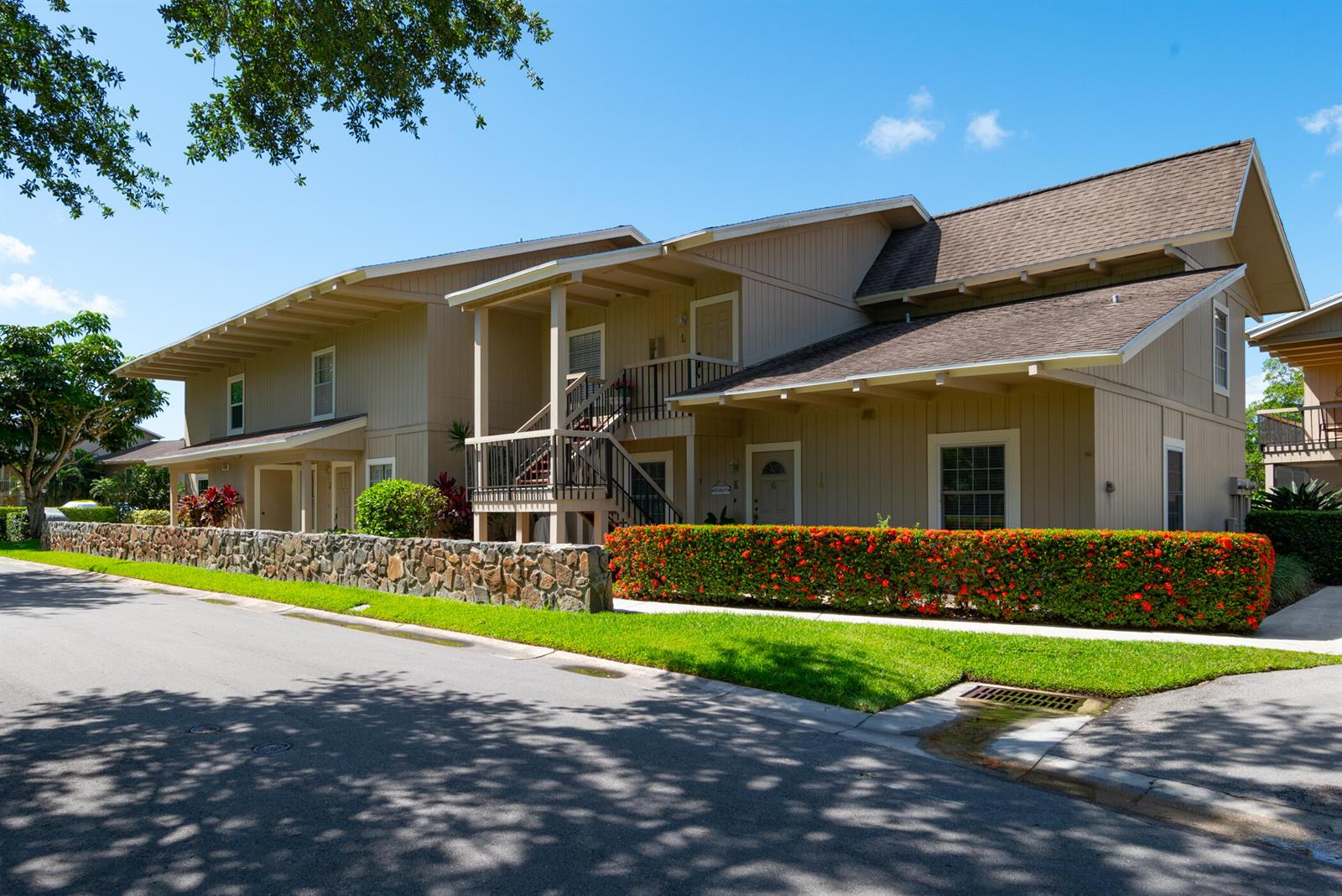 A two-story tan apartment building features a stone wall, red flowering hedges, and stairs — 9130 SE Riverfront Terrace # L, Jupiter FL 33469, JUPITER, FL