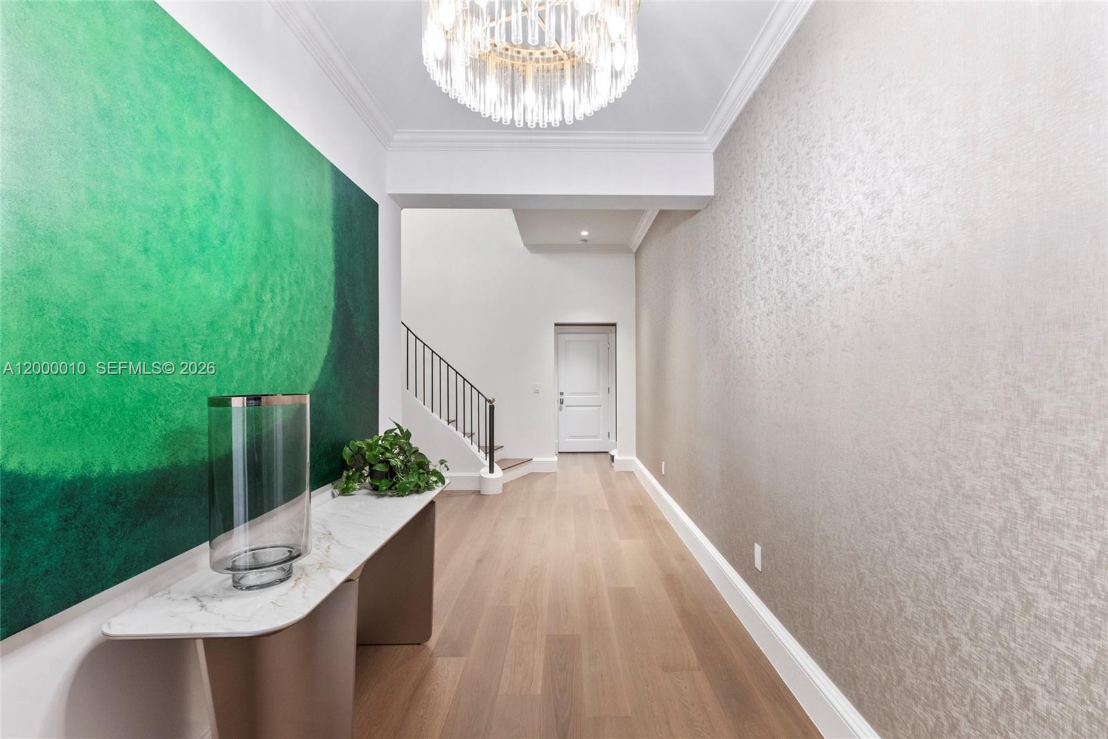 A modern entryway features a green accent wall, a console table, and a crystal chandelier — 2617 Anderson Rd, Coral Gables FL 33134, CORAL GABLES, FL