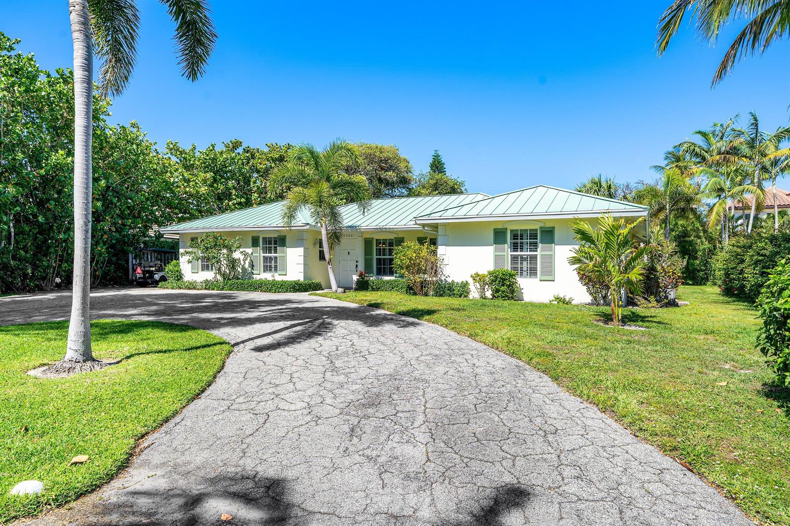 A single-story house with a green metal roof and a cracked asphalt driveway — 5550 Osprey Drive, Ocean Ridge FL 33435, OCEAN RIDGE, FL