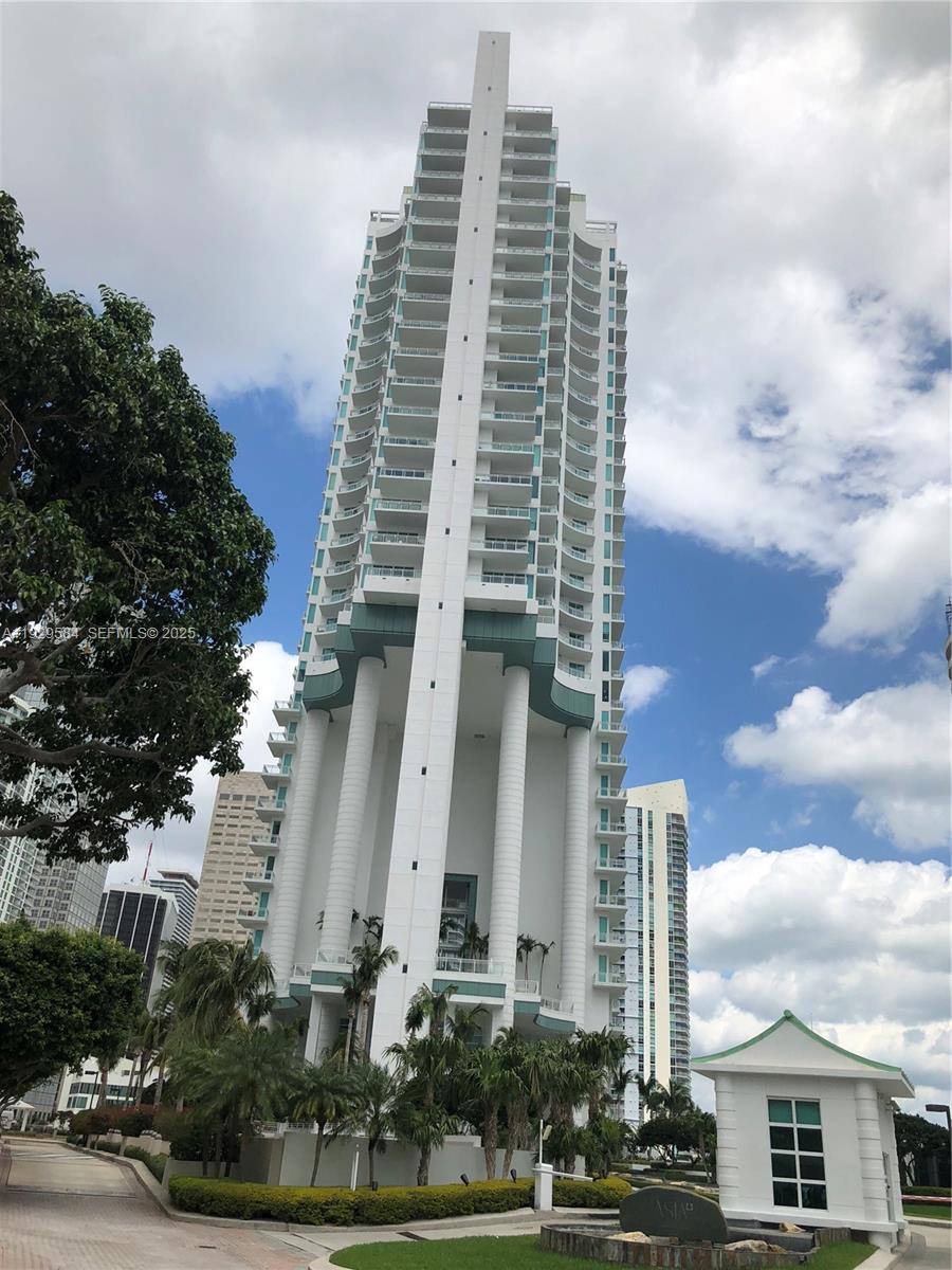 A tall, white residential skyscraper stands prominently against a blue sky with scattered clouds — 900 Brickell Key Blvd # 1602, Miami FL 33131, MIAMI, FL