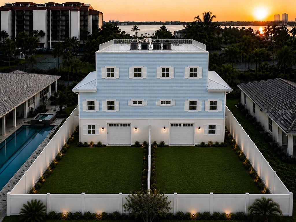 An aerial view of a light blue duplex with two garages and fenced backyards at sunset — 7045 HIBISCUS, SOUTH PASADENA, FL