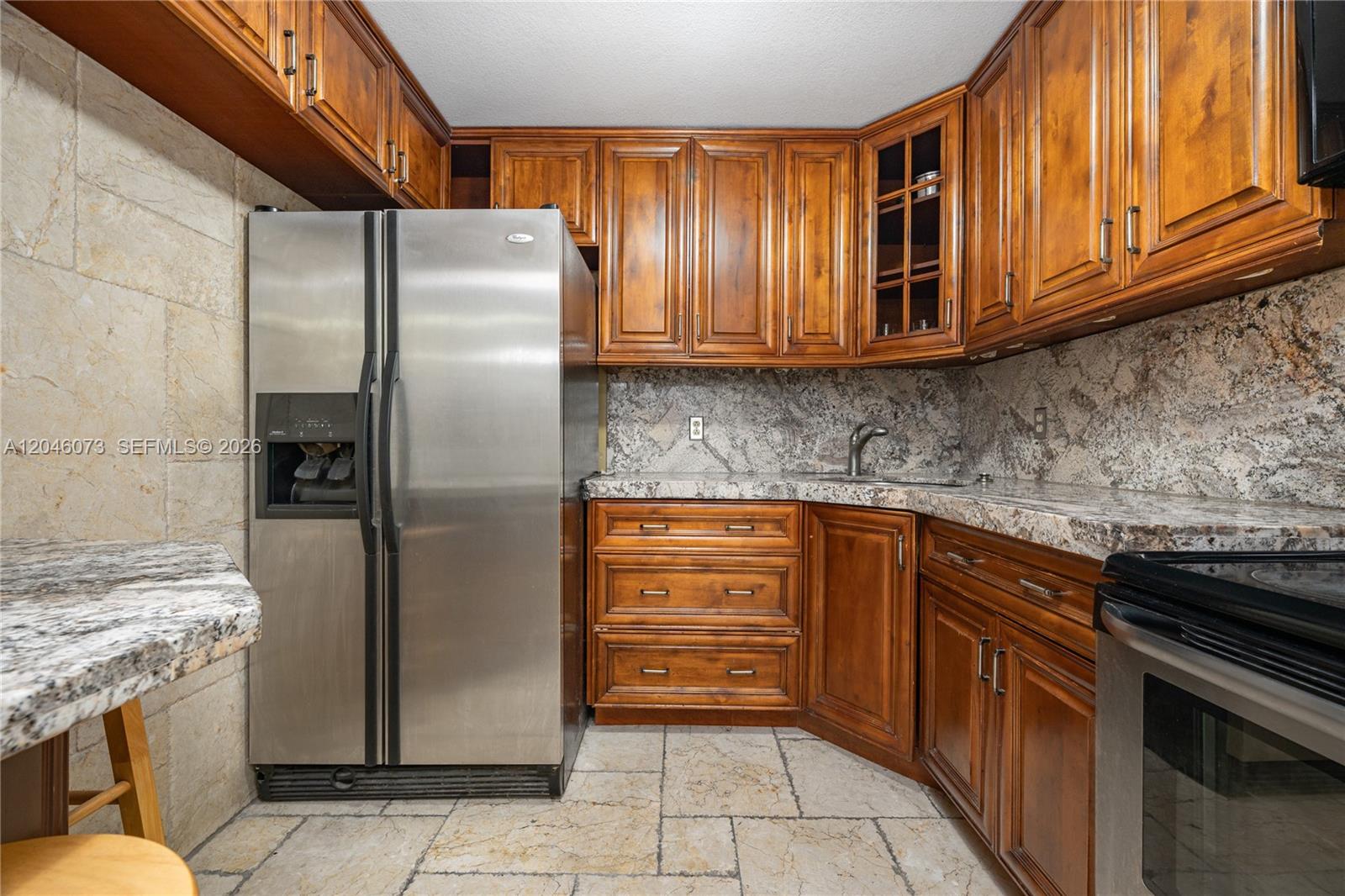 A kitchen features wood cabinets, granite countertops, stainless steel appliances, and stone tile flooring — 701 Three Islands Blvd # 206, Hallandale Beach FL 33009, HALLANDALE BEACH, FL