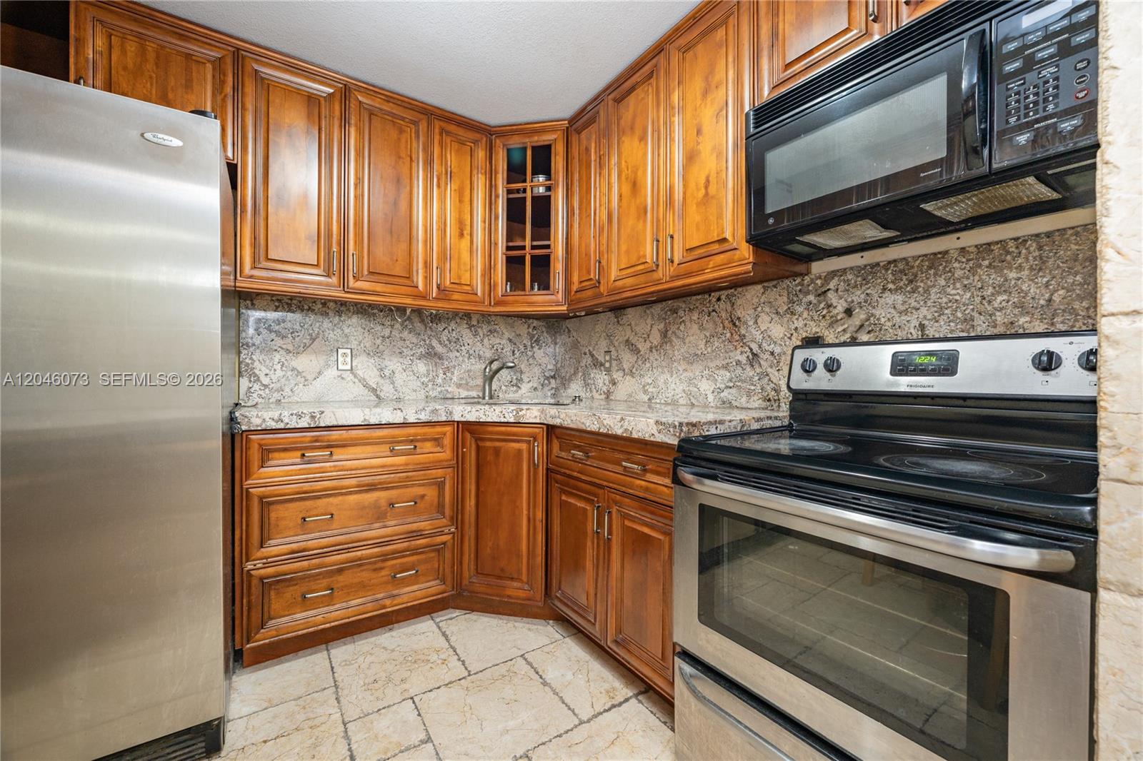 A kitchen features wood cabinets, granite countertops, a stainless steel refrigerator, and a black stove — 701 Three Islands Blvd # 206, Hallandale Beach FL 33009, HALLANDALE BEACH, FL