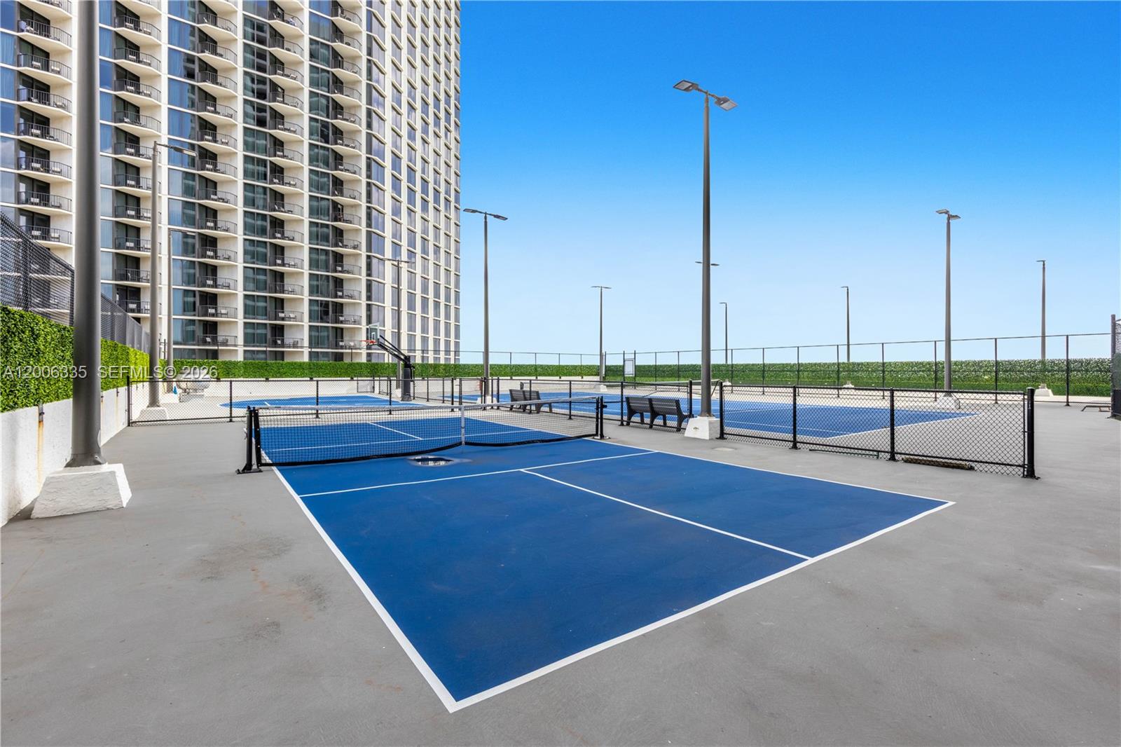 A blue pickleball court with a net sits on a rooftop terrace beside a building — 555 NE 15th St # 501, Miami FL 33132, MIAMI, FL