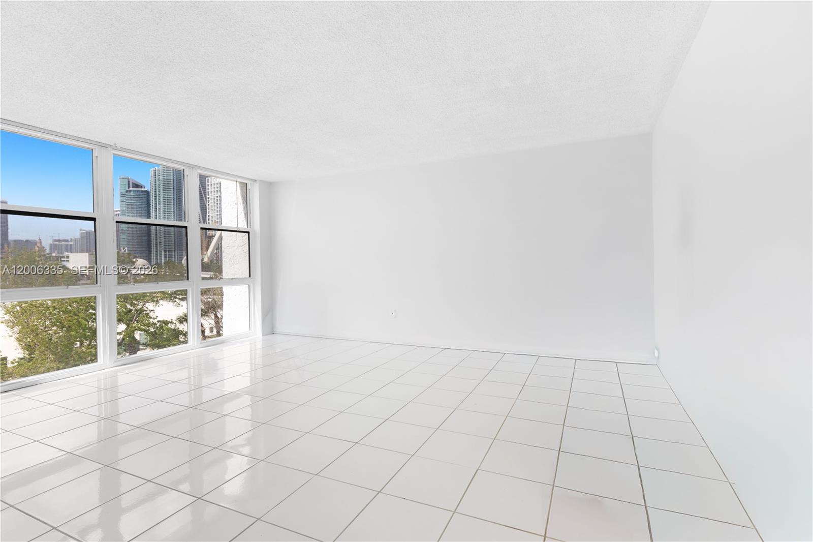 An empty room features white tiled floors, plain white walls, and large floor-to-ceiling windows — 555 NE 15th St # 501, Miami FL 33132, MIAMI, FL