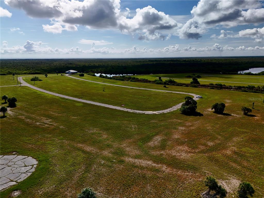 An aerial view shows a paved road winding through a large, grassy, undeveloped rural lot — 12384 BONITA PLACE, PLACIDA, FL