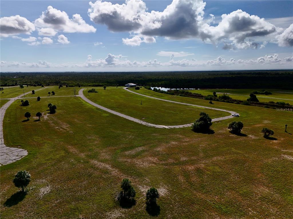 An aerial view shows a paved road winding through a large, grassy, undeveloped lot — 12384 BONITA PLACE, PLACIDA, FL