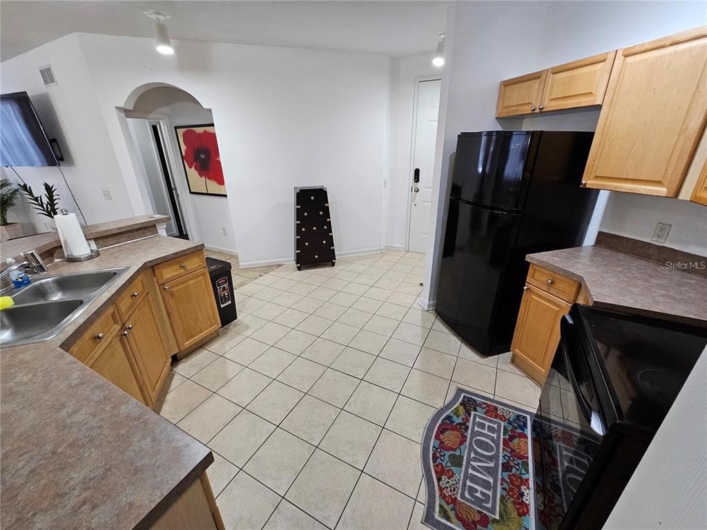 A kitchen features light wood cabinets, black appliances, and beige tile flooring — 202 TERRACE RIDGE CIRCLE UNIT 202, DAVENPORT, FL