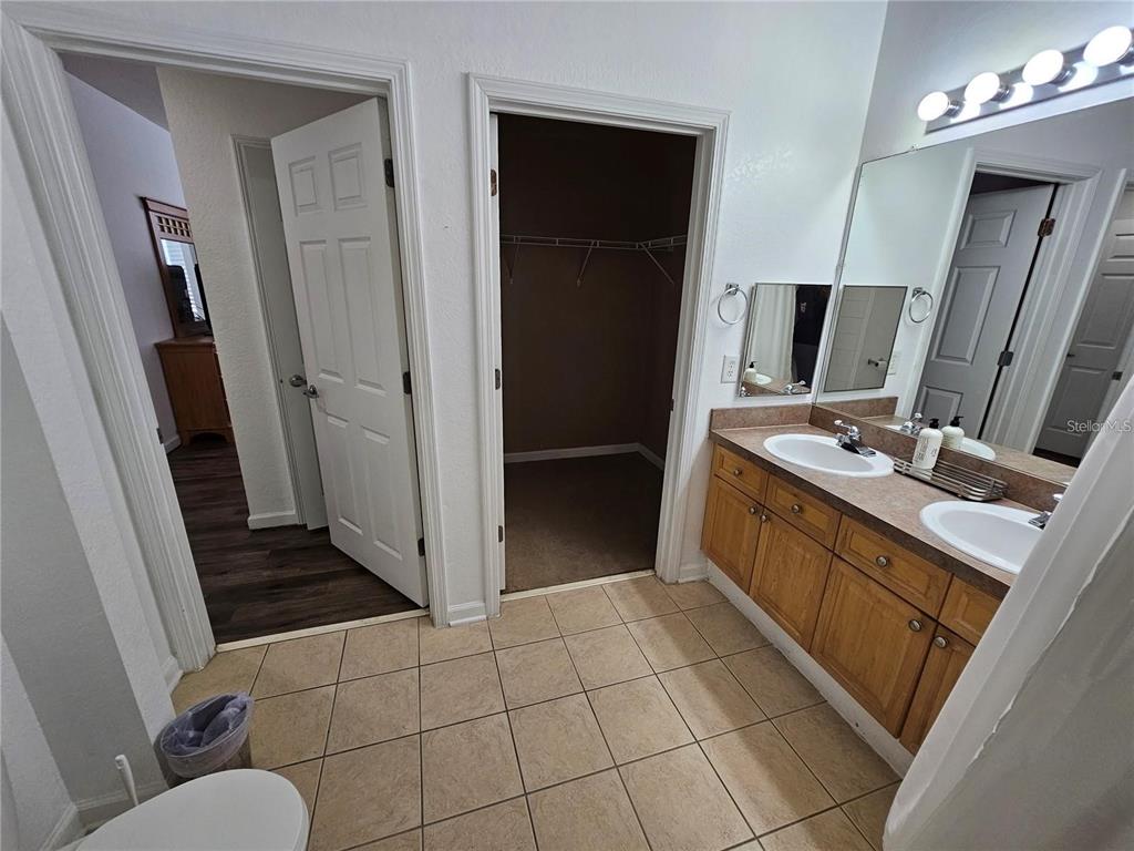A bathroom features a double vanity with wood cabinets, tiled flooring, and an open walk-in closet — 202 TERRACE RIDGE CIRCLE UNIT 202, DAVENPORT, FL