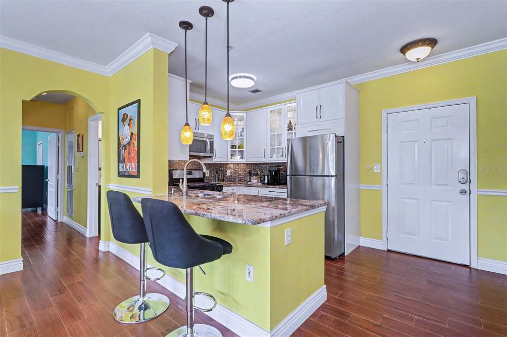 An open-concept kitchen and dining area features yellow walls, wood flooring, and pendant lighting — 2746 VIA TIVOLI UNIT 122B, CLEARWATER, FL