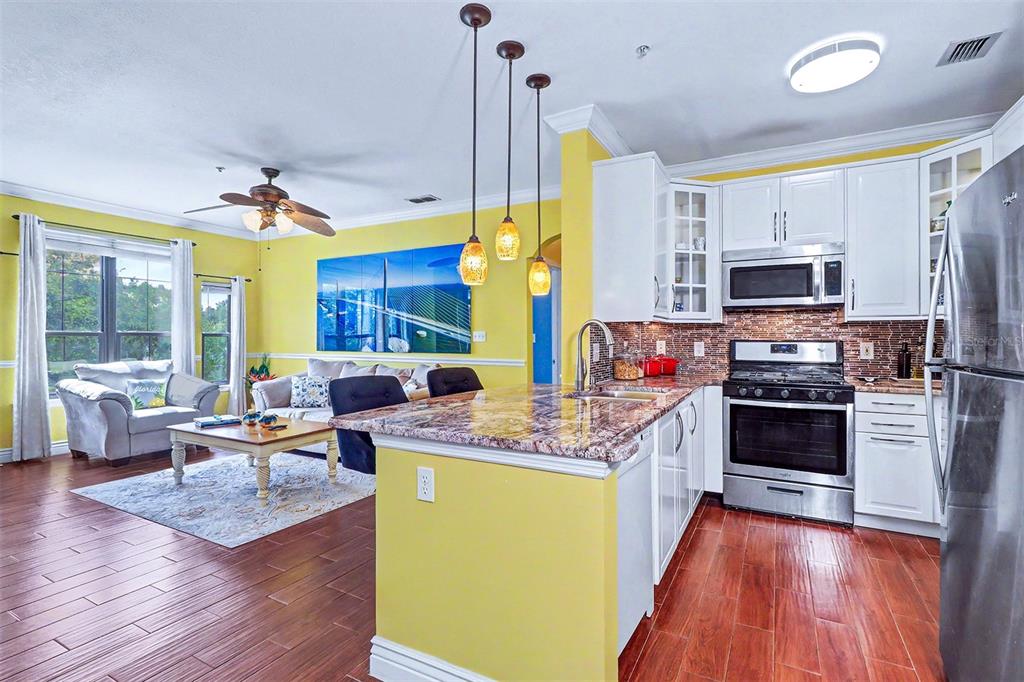 A kitchen features yellow walls, white cabinets, stainless steel appliances, and a granite-topped island — 2746 VIA TIVOLI UNIT 122B, CLEARWATER, FL