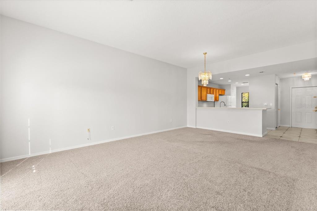 A spacious carpeted living room opens to a kitchen with wooden cabinets and a breakfast bar — 909 WATERSIDE LANE UNIT 307, CELEBRATION, FL