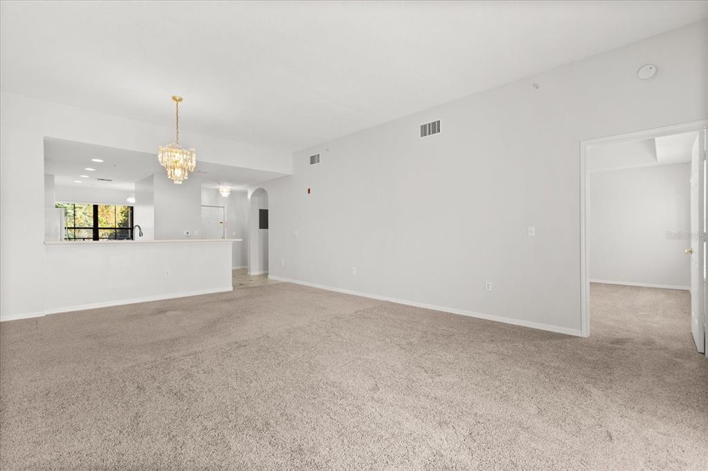 An empty living room features beige carpeting, white walls, and a crystal chandelier — 909 WATERSIDE LANE UNIT 307, CELEBRATION, FL