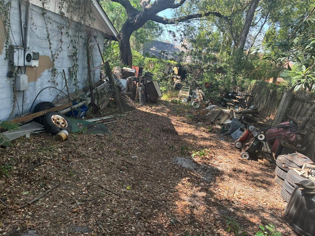 An outdoor side yard filled with debris, old tires, and scattered equipment next to a building — 1309 W RAMBLA STREET, TAMPA, FL