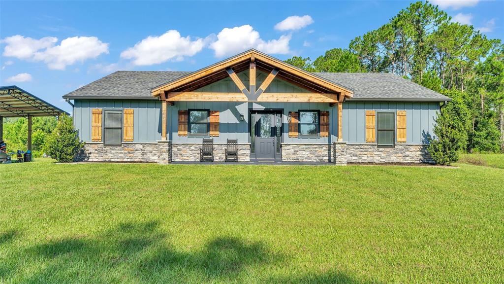 A single-story house with blue board-and-batten siding, stone accents, and a wooden front porch — 18940 COMMONWEALTH AVENUE N, POLK CITY, FL