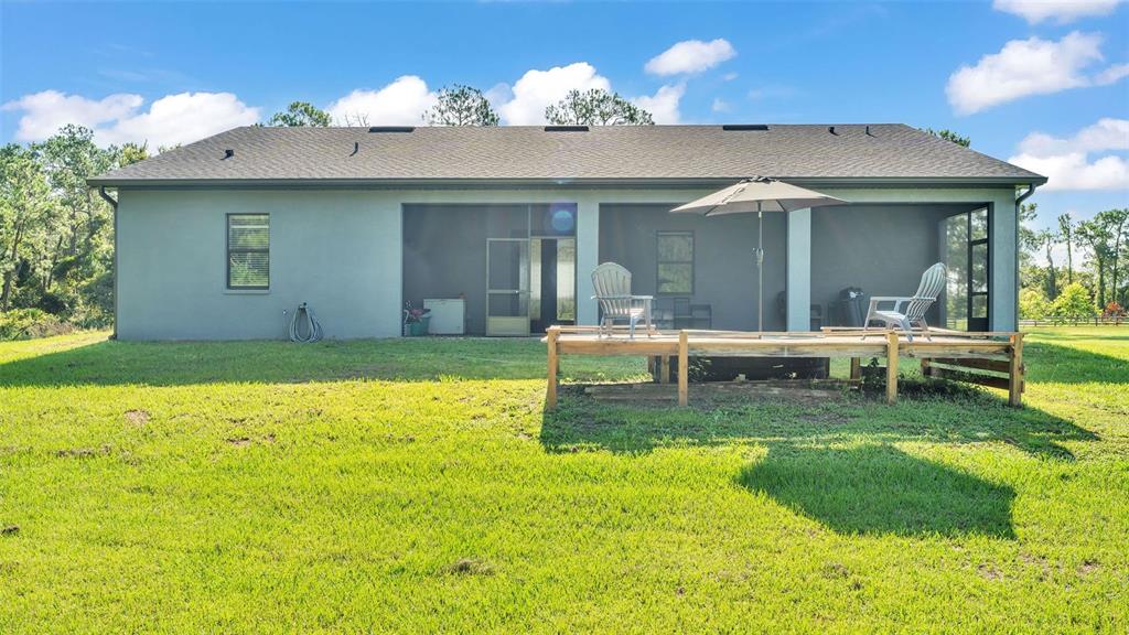 The rear exterior of a house features a screened-in porch and a wooden deck — 18940 COMMONWEALTH AVENUE N, POLK CITY, FL