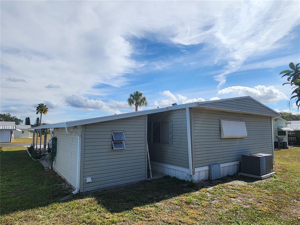 The exterior of a light-colored mobile home features vinyl siding, a metal awning, and an AC unit — 188 SWEET CIRCLE DRIVE, WINTER HAVEN, FL