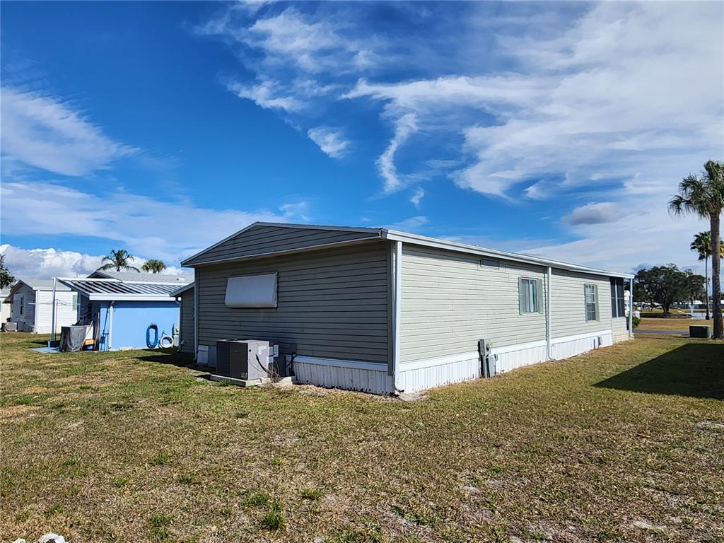 A side view of a light-colored mobile home with gray siding and a central air unit — 188 SWEET CIRCLE DRIVE, WINTER HAVEN, FL