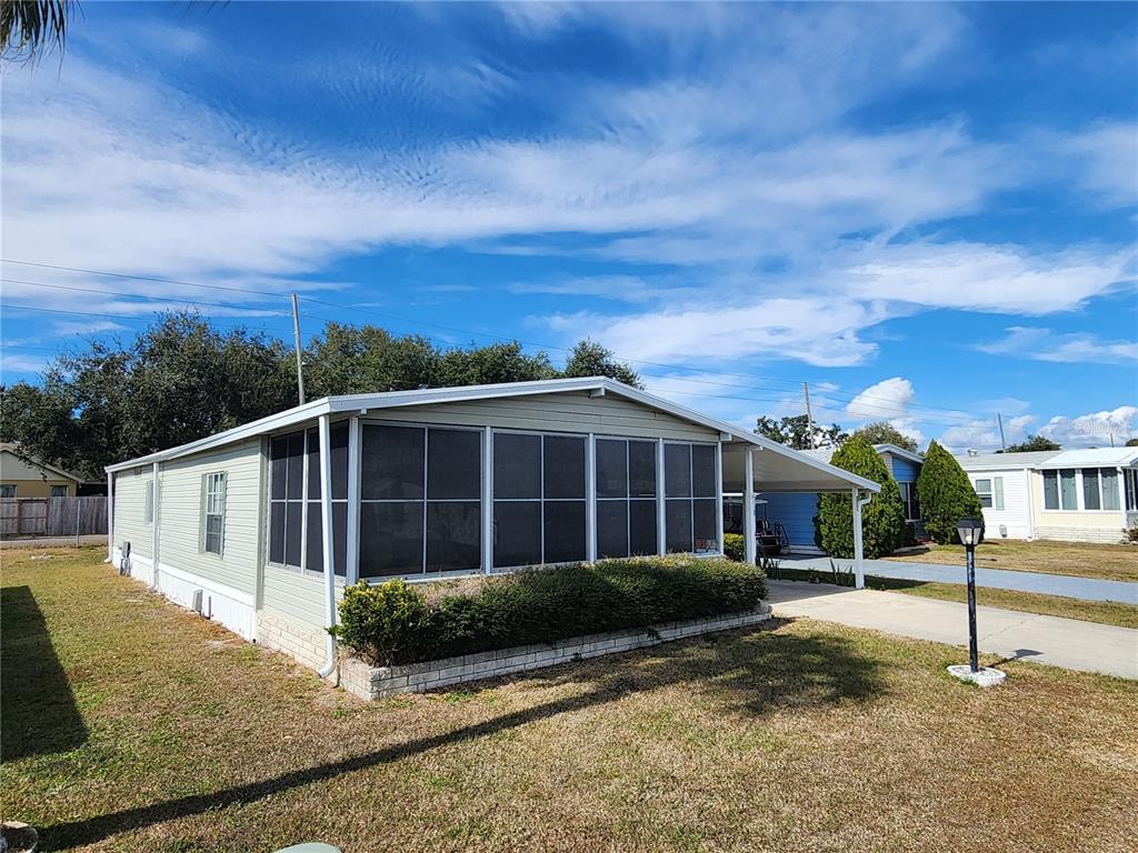 A light green mobile home features a large screened-in front porch and a concrete driveway — 188 SWEET CIRCLE DRIVE, WINTER HAVEN, FL