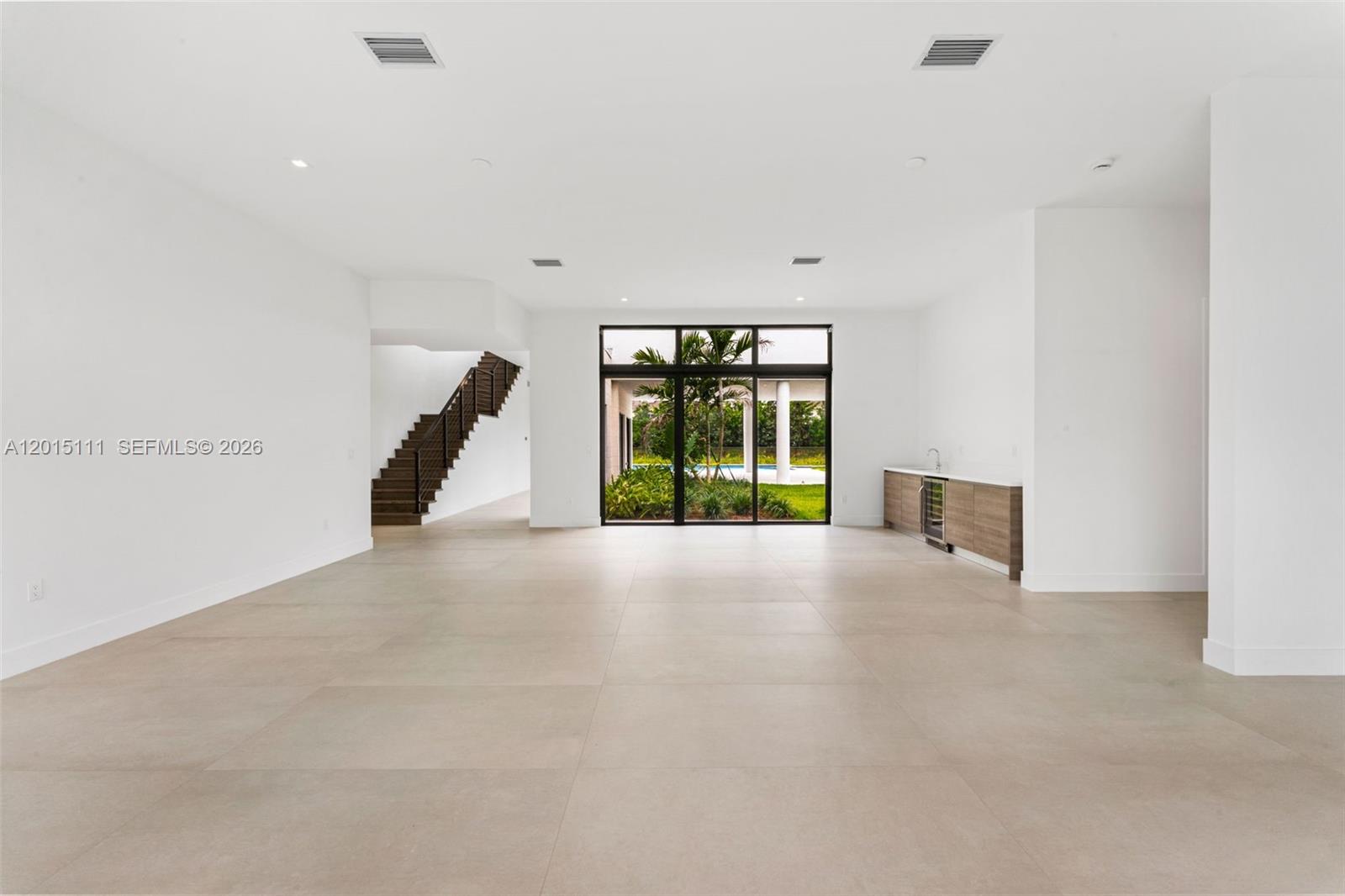 A spacious, minimalist room features large floor tiles, a staircase, and a wet bar area — 16700 N Botaniko Dr N, Weston FL 33326, WESTON, FL