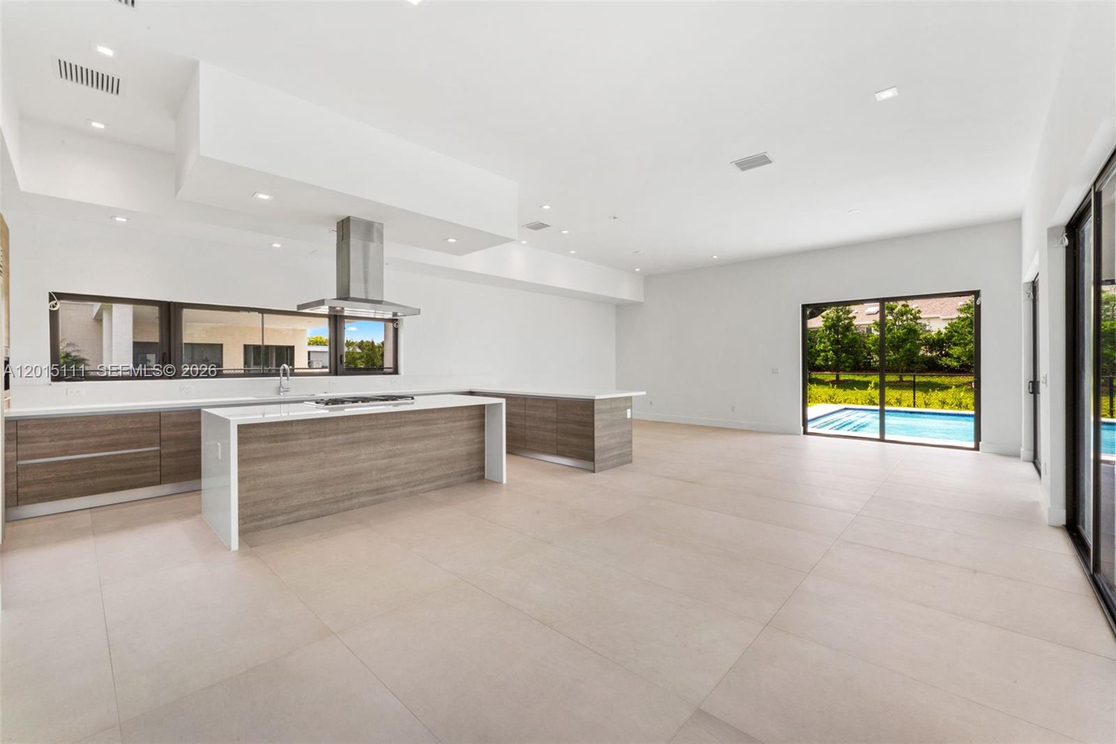 A modern kitchen with wood-toned cabinetry and a white island overlooks a backyard swimming pool — 16700 N Botaniko Dr N, Weston FL 33326, WESTON, FL