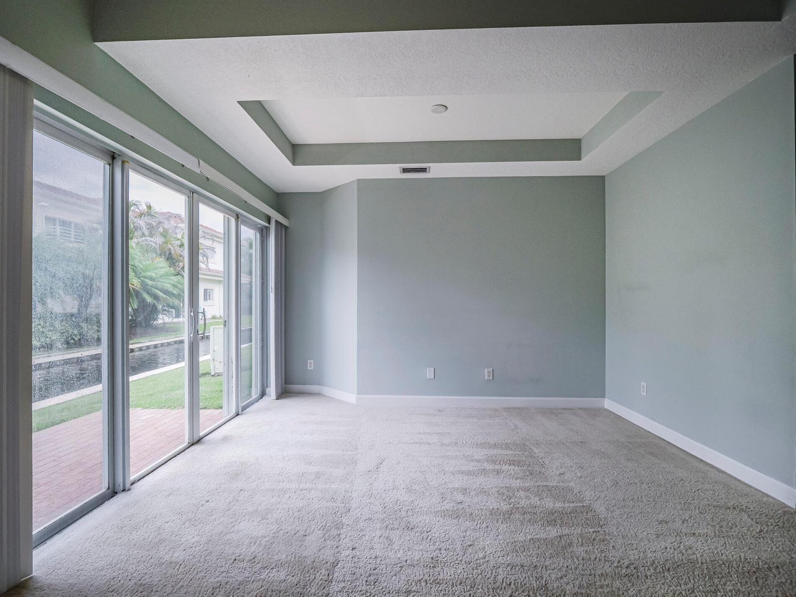 An empty room with light blue walls, beige carpeting, a tray ceiling, and sliding glass doors — 524 7th Square # 101, Vero Beach FL 32962, VERO BEACH, FL