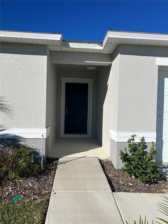 A concrete walkway leads to the dark front door of a light-colored stucco house — 604 SARNER PASS WAY, WINTER HAVEN, FL
