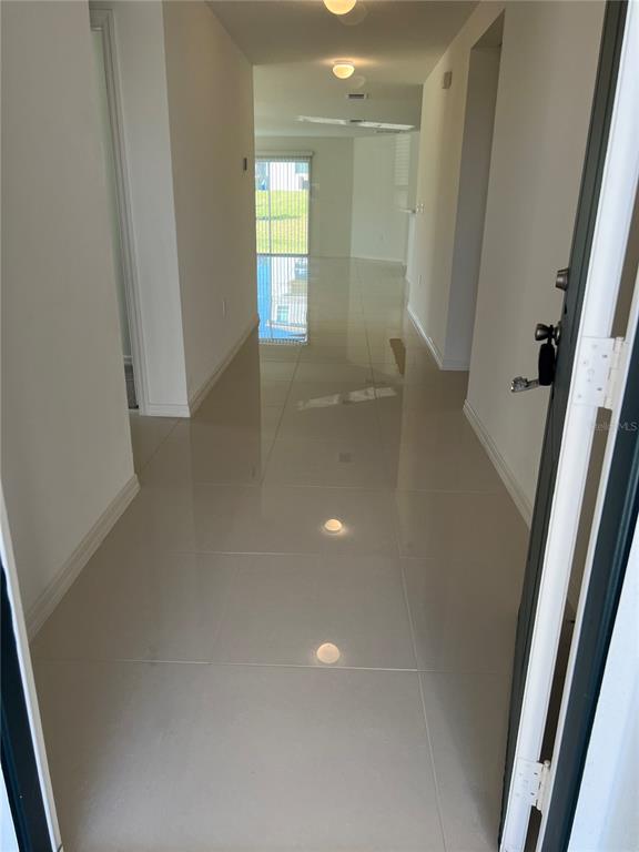 A bright hallway with light-colored tile flooring leads toward a glass sliding door — 604 SARNER PASS WAY, WINTER HAVEN, FL