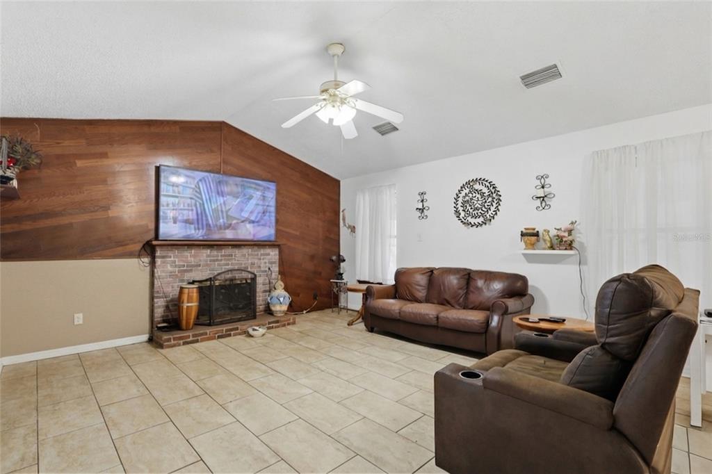 A living room features a brick fireplace, wood-paneled accent wall, tile flooring, and leather furniture — 11808 FAWN DALE DRIVE, RIVERVIEW, FL
