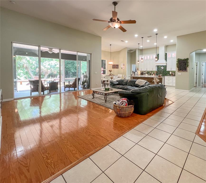 An open-concept living room with hardwood floors, a leather sofa, and sliding glass patio doors — 9046 SHENANDOAH RUN, WESLEY CHAPEL, FL