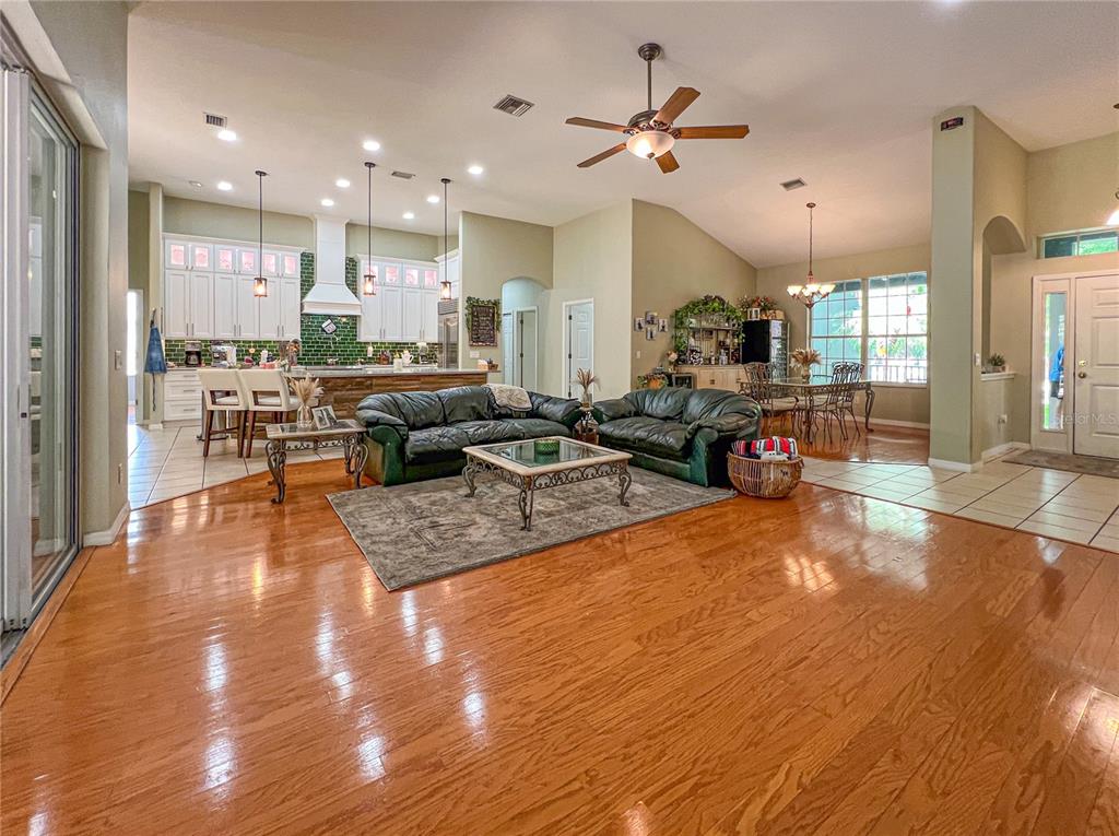 An open-concept living room and kitchen featuring hardwood floors, dark leather sofas, and white cabinetry — 9046 SHENANDOAH RUN, WESLEY CHAPEL, FL