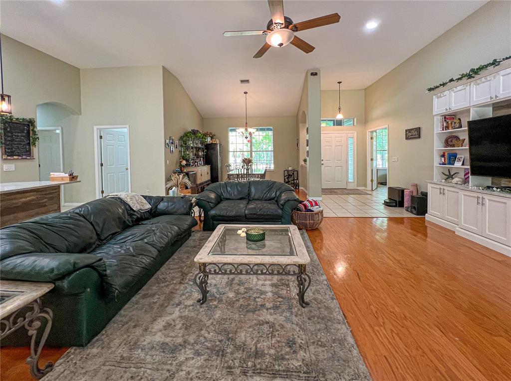 A living room features dark leather sofas, a glass-top coffee table, and hardwood flooring — 9046 SHENANDOAH RUN, WESLEY CHAPEL, FL