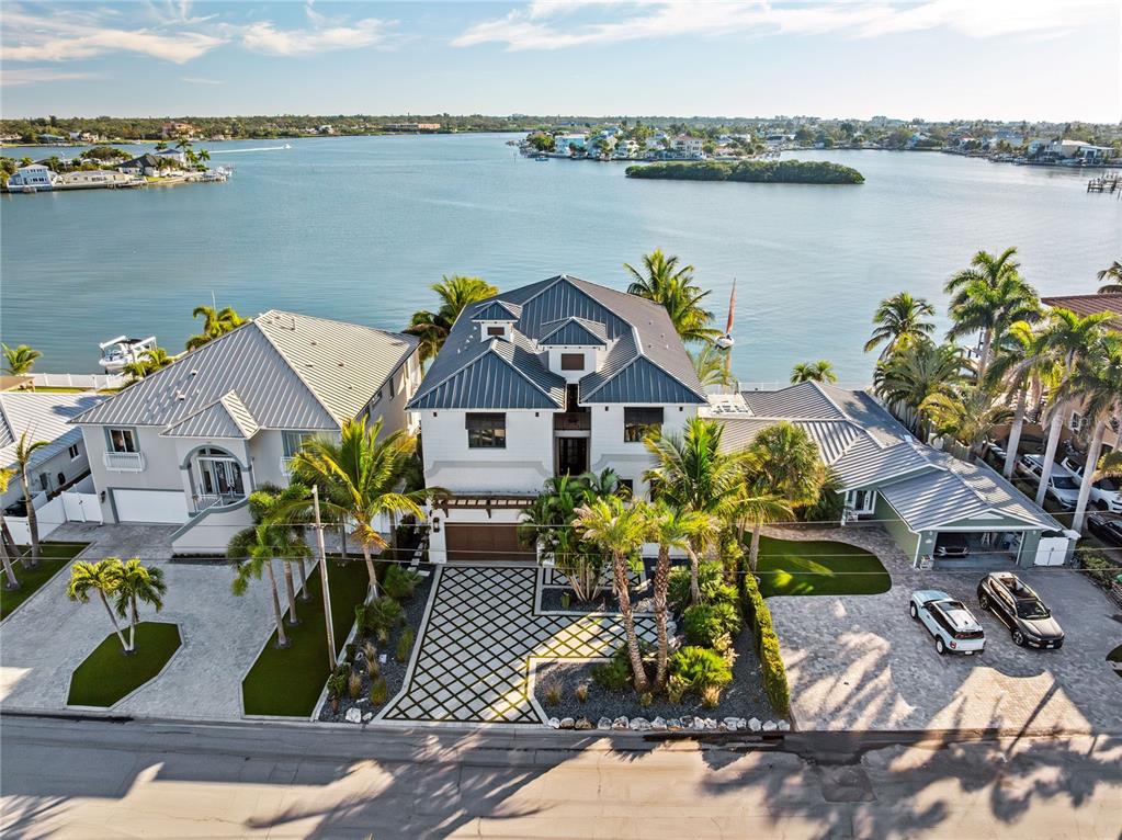An aerial view shows three waterfront houses with metal roofs and palm trees along a bay — 459 20TH AVENUE, INDIAN ROCKS BEACH, FL