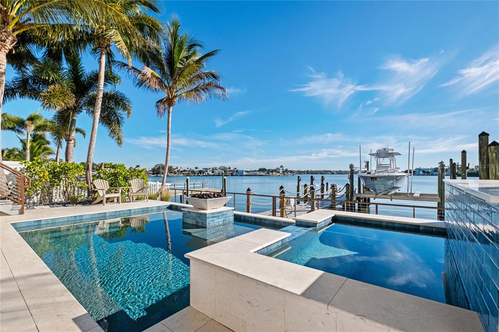 A swimming pool and spa overlook a waterfront dock with a boat under a blue sky — 459 20TH AVENUE, INDIAN ROCKS BEACH, FL