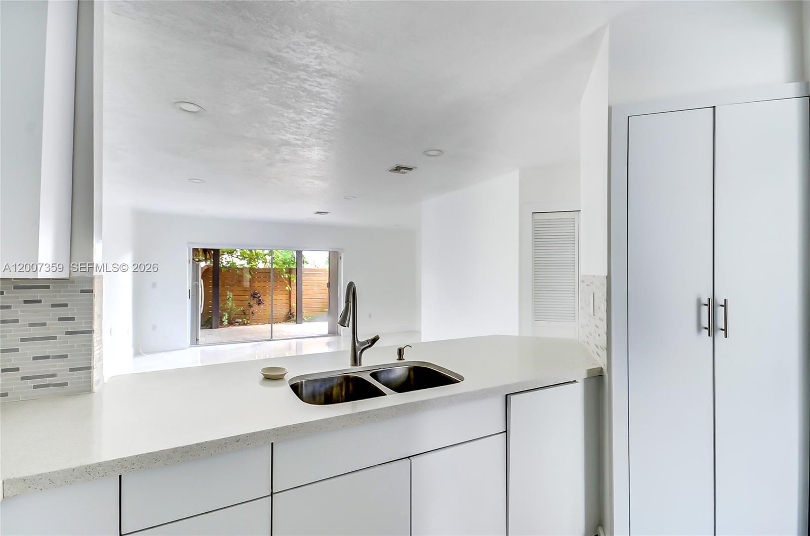A kitchen with white cabinets, a double sink, and a view of a backyard patio — 12909 SW 61 # 0, Miami FL 33183, MIAMI, FL