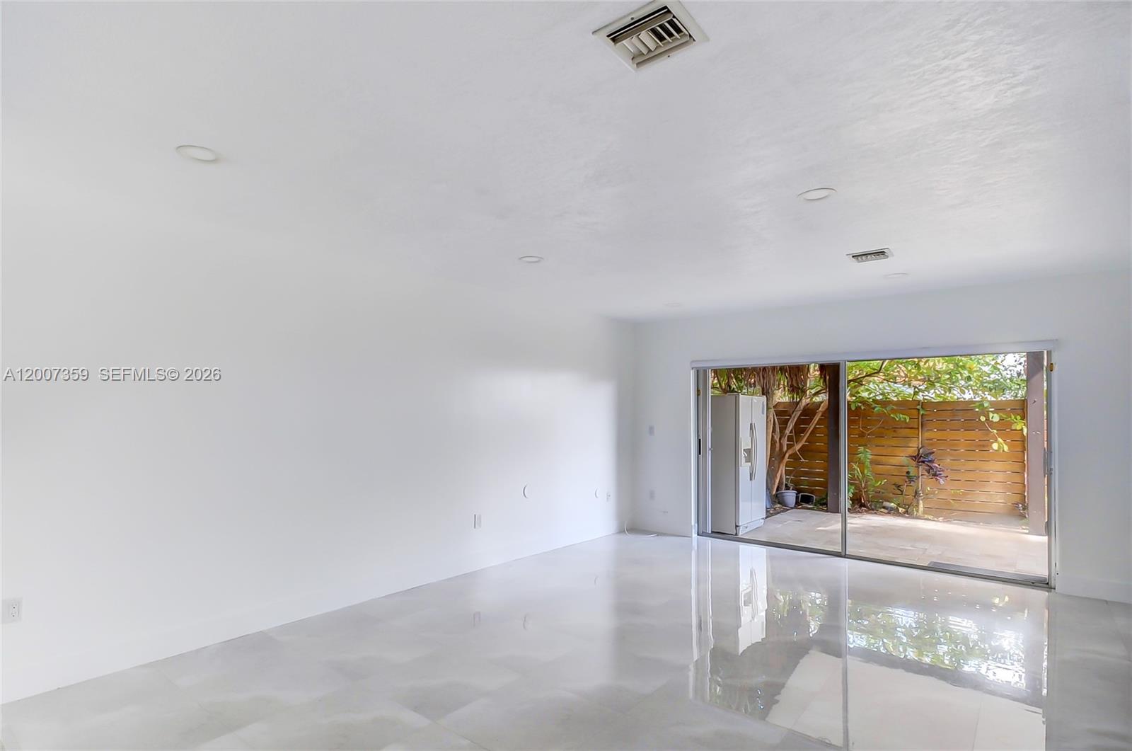 A bright, empty room features white walls, glossy tiled floors, and sliding glass doors to a patio — 12909 SW 61 # 0, Miami FL 33183, MIAMI, FL