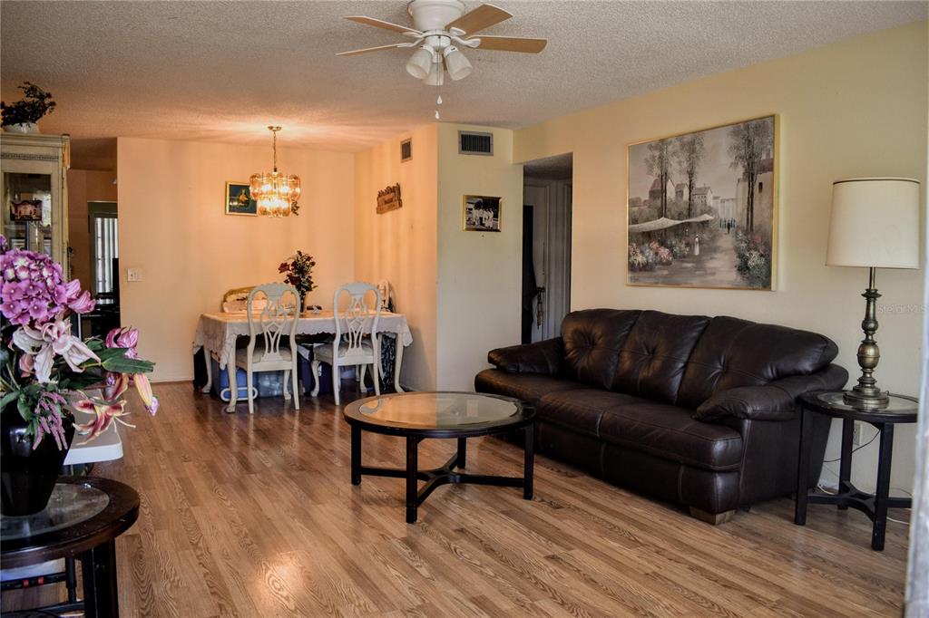 A living and dining area features wood-look flooring, a dark leather sofa, and a ceiling fan — 2370 JAMAICAN STREET UNIT 54, CLEARWATER, FL