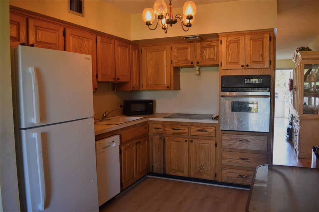 A kitchen features oak cabinets, a white refrigerator, a built-in oven, and a chandelier — 2370 JAMAICAN STREET UNIT 54, CLEARWATER, FL