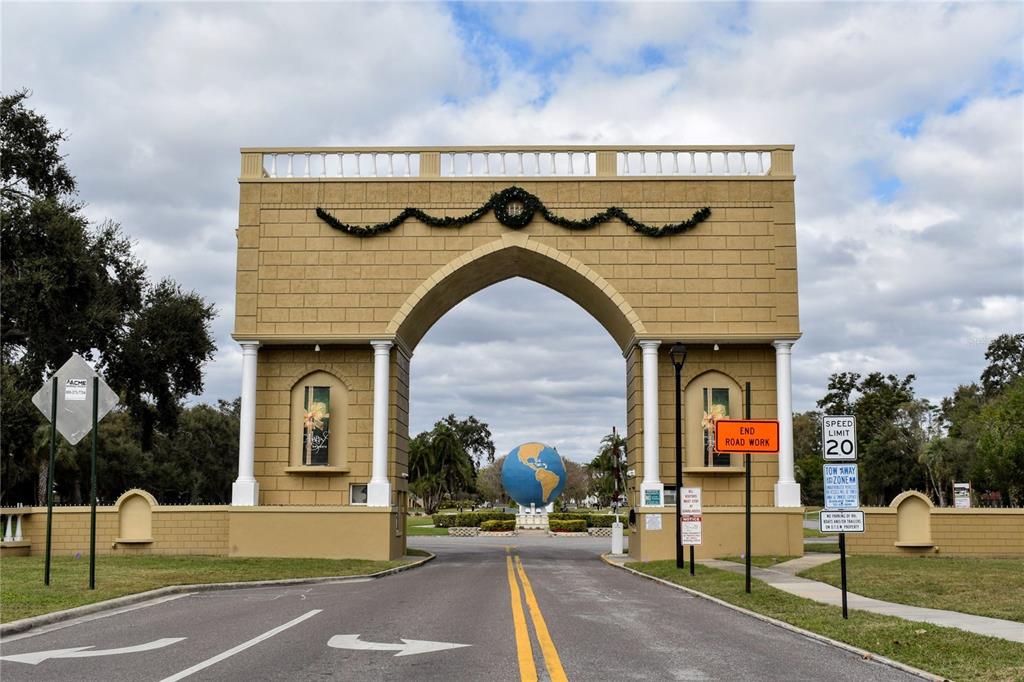 A large, tan, arched stone entrance gate stands over a road leading to a globe sculpture — 2370 JAMAICAN STREET UNIT 54, CLEARWATER, FL