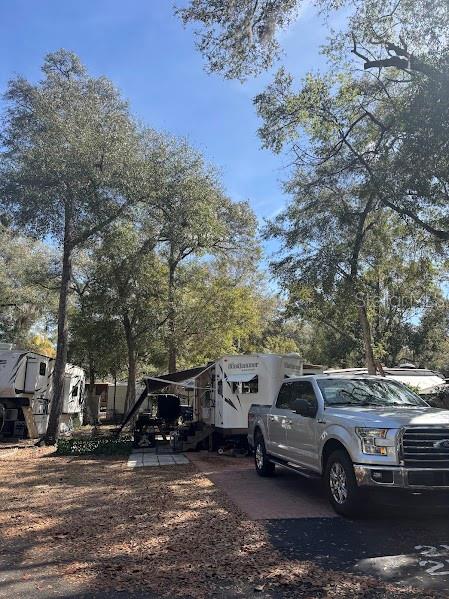 A silver pickup truck is parked next to a white recreational vehicle under large trees — 25188 NE 142ND PLACE UNIT 219, FORT MC COY, FL