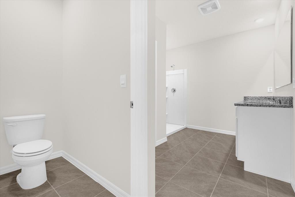 A bathroom features a toilet in a separate alcove, a vanity, and a walk-in shower — 5209 BAROMBI BEND, ST CLOUD, FL