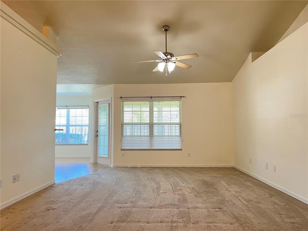 A carpeted living room features a vaulted ceiling, a ceiling fan, and large windows — 19430 NW 164TH ROAD, HIGH SPRINGS, FL